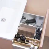 Stilfull baderomsinspirasjon med beige servantskap med innerskuff, overskap, åpen hylle, ovalt speil med belysning, matchende pendler, hylle under speilet, og vegghengt toalett. Vegger med lyse, avlange fliser