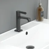 Stilfull baderomsinspirasjon med beige servantskap med innerskuff, overskap, åpen hylle, ovalt speil med belysning, matchende pendler, hylle under speilet, og vegghengt toalett. Vegger med lyse, avlange fliser