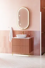 Stort vintage retro baderomsinspirasjon med terrakottafarget servantskap med riller, elegant tynn benkeplate og vakker bordstående servant, stilfullt ovalt speil med messingkant. Lyserosa fliser og grå sildebensfliser gir et romantisk og feminint uttrykk
