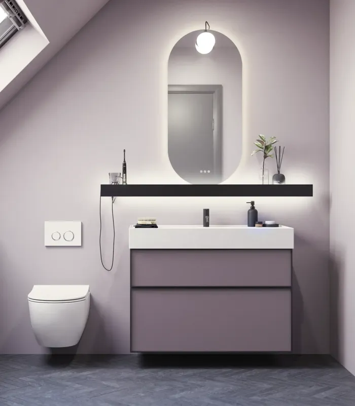 Baderom med skrå vegger inspirasjon, med baderomsmøbler i lilla med elegante rammefronter, flott oval speil med lampe, vakker og praktisk hylle, samt lilla malt vegg og grått fiskebeinsgulv som gir et elegant og moderne uttrykk.