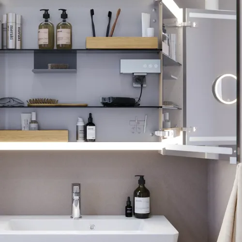 Liten baderomsinspirasjon med servantskap og overskap over toalett i beige spesialfarge, elegant speilskap med integrert lys, de lyse fargene og hvite gardinet skaper en romantisk og feminin atmosfære.