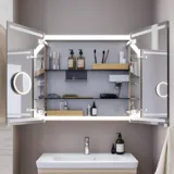 Liten baderomsinspirasjon med servantskap og overskap over toalett i beige spesialfarge, elegant speilskap med integrert lys, de lyse fargene og hvite gardinet skaper en romantisk og feminin atmosfære.