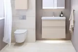 Liten baderomsinspirasjon med servantskap og overskap over toalett i beige spesialfarge, elegant speilskap med integrert lys, de lyse fargene og hvite gardinet skaper en romantisk og feminin atmosfære.