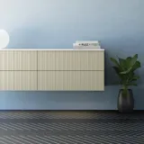 Baderom med skrått tak inspirasjon, beige baderomsmøbler med rifler, elegant benkeplate og firkantet bordstående servant, vakkert firkantet speil med stilige hyller, blå vegger, store vinduer og sort fiskebeinsgulv gir et lyst og urbant uttrykk.