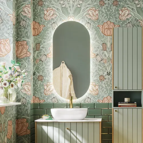 Baderomsinspirasjon med baderomsmøbler i grønn spesialfarge med sider i naturlig eik, elegante riller, stilfull benkeplate med romantisk oval bordstående servant, vakkert ovalt speil, gir sammen med blomstrete tapet et yndefullt, vintage retro uttrykk.
