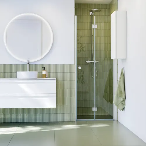 Baderomsinspirasjon med hvite baderomsmøbler, elegant rundt speil og dusjnisje med foldedør i klart glass og profiler i sateng, grønne avlange fliser gir et sofistikert uttrykk.