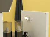 Liten baderomsinspirasjon med hvitt vaskeskap med svart grep og svart elegant vask, vakkert rundt speil med svart kant, forskjøvet plasserte overskap samt terrazzo vegg og gulv og gule vegger gir et modig og moderne uttrykk.