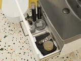 Liten baderomsinspirasjon med hvitt vaskeskap med svart grep og svart elegant vask, vakkert rundt speil med svart kant, forskjøvet plasserte overskap samt terrazzo vegg og gulv og gule vegger gir et modig og moderne uttrykk.