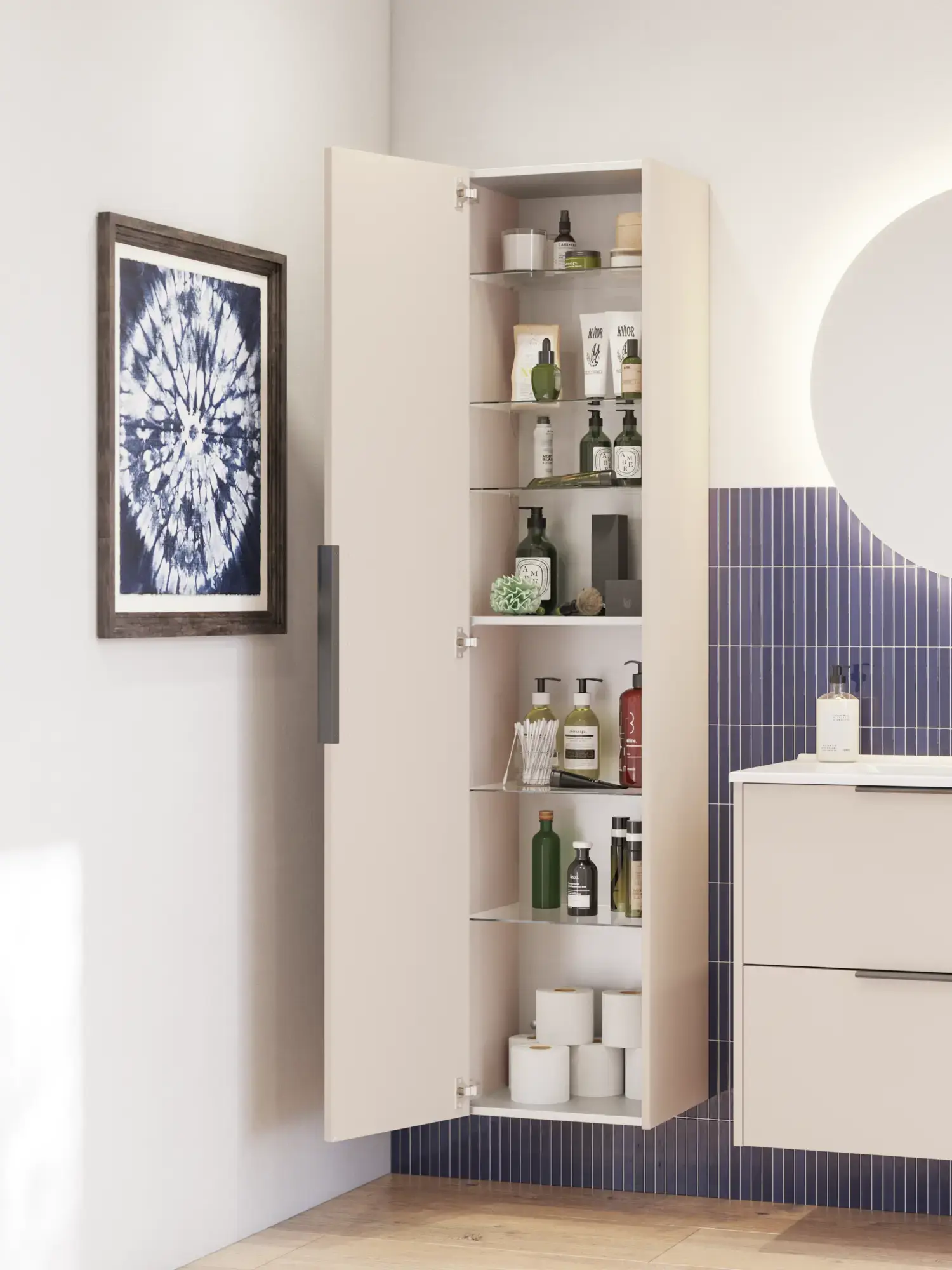 Baderomsinspirasjon med avlange blå fliser, elegant beige servantskap og høyskap med svarte, minimalistiske og avlange håndtak og et rundt speil med lys som gir et vakkert og kontrastfylt uttrykk.