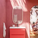 Baderomsinspirasjon med røde vegger, mykt formede røde servantskap og høyskap, elegant hvit servant og et vakkert ovalt speil med lys som sammen med de naturlige omgivelsene skaper et vintage uttrykk